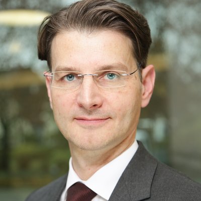 Portrait von Dr. Stefan Hoehl, ein dunkelhaariger Herr mit Brille, Anzug und roter Krawatte, ca. Ende vierzig