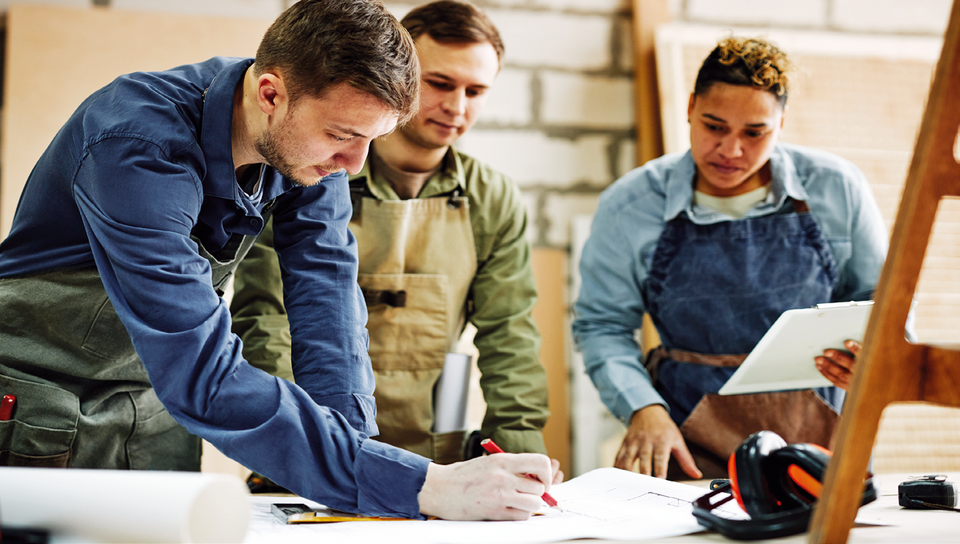 Drei Menschen, die im Handwerk arbeiten, planen etwas an einem Tisch