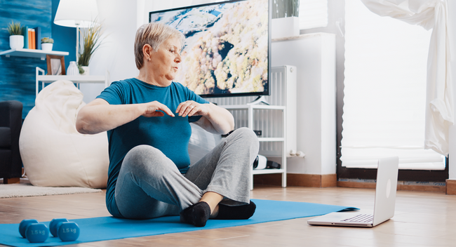 Seniorin macht zuhause Sport vor einem Laptop